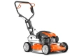 Kosiarka spalinowa Husqvarna LB553SQe w kolorze pomarańczowym; widok z boku. Z przodu srebrne koła, metalowa podstawka. Widoczny silnik i rączka, która jest rozłożona. Tło proste, czarne, co podkreśla wygląd produktu.