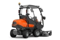 Rider Profesjonalny P525DX z kabiną Husqvarna w kolorze pomarańczowym z ciemnoszarymi elementami. Ujęcie z boku, złożony, widoczne koła, przeszklona kabina, oraz wyposażenie do koszenia. Logo Husqvarna widoczne na obudowie.