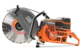 Zagęszczarka Husqvarna LT 6005 w pomarańczowo-szarym kolorze, z dużą tarczą tnącą, logiem Husqvarna i bieżnią odprowadzającą pył. Widok z boku, uchwyt u góry, na prostym tle.