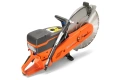Zagęszczarka Husqvarna LT 6005 w kolorze pomarańczowym z szarym silnikiem, z widocznym kołem tnącym. Ujęcie frontalne ukazuje ergonomiczne uchwyty i panel sterujący z oznaczeniami funkcji. Tło czarne, skupiające uwagę na produkcie.