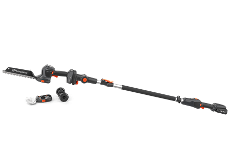 Nożyce do krzewów Husqvarna Aspire™ SE20-P4A na wysięgniku, czarne z pomarańczowymi akcentami. Stojący, z bliska; widoczny mechanizm tnący oraz uchwyt. W zestawie mały wymienny osprzęt. Tło przezroczyste.