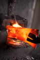 Zgrzewany metal w ogniu na kowadle, o intensywnej czerwonej barwie. Widać dym unoszący się z gorącej powierzchni, kształt metalu jest nieregularny, a obok widoczny uchwyt narzędzia. Ujęcie zbliżone, z różnymi materiałami w tle.