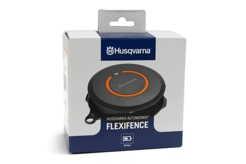 Husqvarna Automower FlexiFence w opakowaniu; okrągły, ciemnoszary z pomarańczowym przyciskiem; oznaczenia na białym tle, widoczny logo Husqvarna; ujęcie frontalne, produkt ustawiony na płaskiej powierzchni.