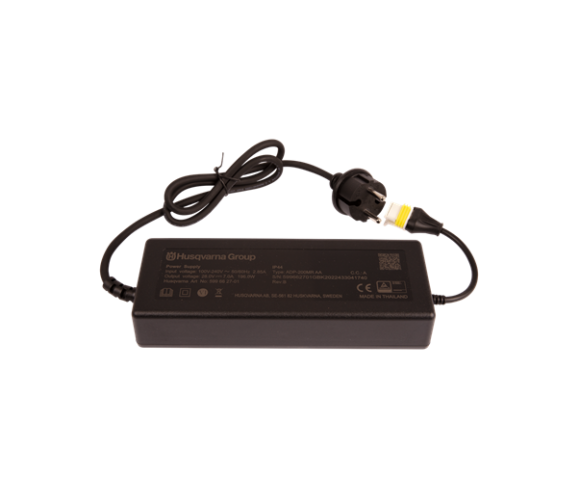 Zasilacz Husqvarna 7.0A, prostokątny, matowy, czarny. Widoczny kabel z wtyczką i gniazdem do podłączenia. Logo Husqvarna na obudowie. Ujęcie z góry, leżący na białym tle, z wyraźnie widocznymi oznaczeniami technicznymi.