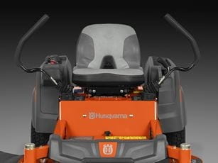 Kosiarka Husqvarna Z242F z silnikiem Kawasaki. Widok frontalny, siedzisko w szaro-pomarańczowym kolorze, z ergonomicznymi uchwytami po bokach, przyciski kontrolne na panelu. Tło ciemne, produkt w pozycji stojącej, dobrze widoczny.