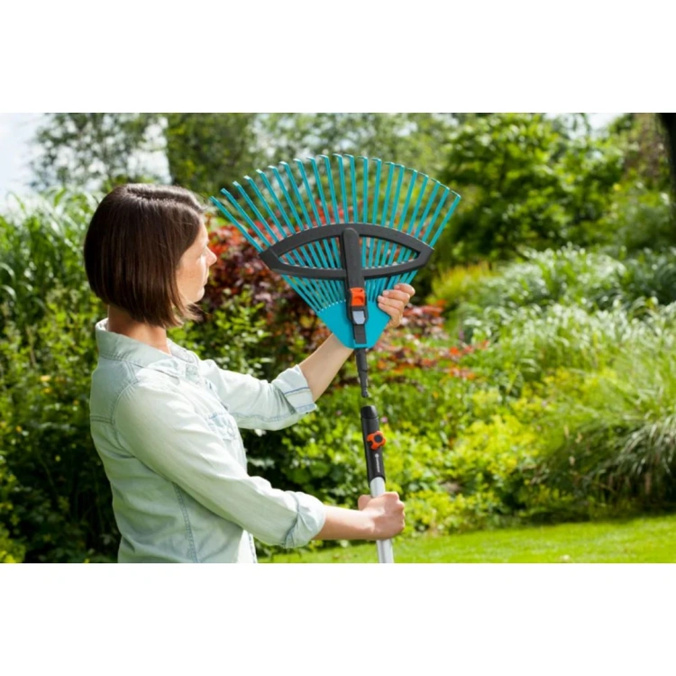 Grabie wachlarzowe regulowane Gardena w kolorze niebieskim, o szerokości od 35 do 52 cm, trzymane przez kobietę. Produkt ukazany z boku, w otoczeniu ogrodu. Widać detal regulacji uchwytu oraz charakterystyczne, elastyczne zęby grabie.