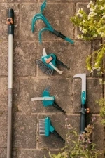 Trzonek drewniany FSC 100% Gardena, długość 150 cm, umieszczony na ziemi obok zestawu narzędzi ogrodowych. Widoczne akcesoria w odcieniach turkusu i czerni, w tym szczotki i zraszacz. Tło z kostki brukowej oraz zielonymi roślinami.
