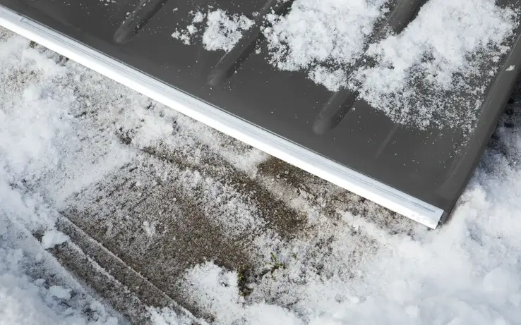 Szufla do śniegu Gardena ClassicLine w kolorze szaro-srebrnym, widoczna na tle zaśnieżonej powierzchni. Ujęcie z boku, pokazujące krawędź roboczą z metalowym wzmocnieniem oraz teksturowaną powierzchnię.