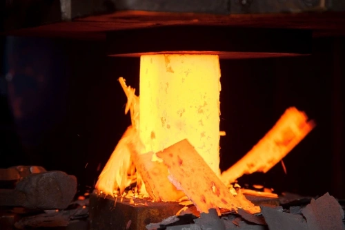 Łopata do nasadzeń Krumpholz z trzonkiem T, metalowa, matowa, stabilna stojąc. W tle iskrzące ziarna metalu i inne narzędzia, podświetlane ciepłym światłem, symbolizujące pracę w warsztacie.