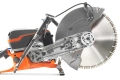 Husqvarna K 970 Rescue z metalową tarczą 350 mm, widoczny pomarańczowo-czarny silnik. Detale mocowania i system napędowy. Jasne tło podkreśla produkt.