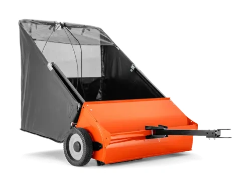 Pomarańczowy zbieracz do trawy Husqvarna 42 z czarną osłoną, dwoma kółkami, zaokrąglonym zbiornikiem i uchwytem do montażu. Tkanina osłony przylega do konstrukcji, wewnątrz przestrzeń na trawę.