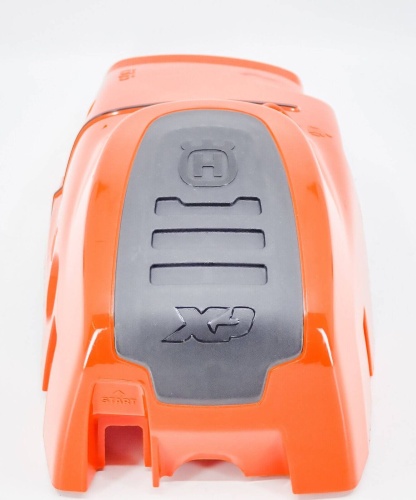 Pokrywa cylindra pilarki Husqvarna 562XP w intensywnym pomarańczowym kolorze, z czarnym logo XP. Przedmiot widoczny z przodu, z detalami w postaci rowków na powierzchni. Na dolnej krawędzi widoczny napis START. Tło białe, co podkreśla produkt.