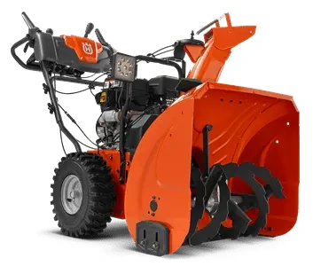 Odśnieżarka ST230 Husqvarna w kolorze pomarańczowym z czarnymi detalami. Produkt stoi na czterech kołach, widoczny jest uchwyt oraz silnik. Zbliżenie na szeroki wyrzutnik śniegu i śruby mocujące. Tło jednolite, podkreślające detale.