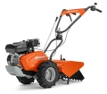 Pomarańczowy kultywator TR 348 Husqvarna z metalową konstrukcją, szerokimi kołami, silnikiem, regulowanym uchwytem i kopaczką z przodu na czarnym tle podkreślającym detale.