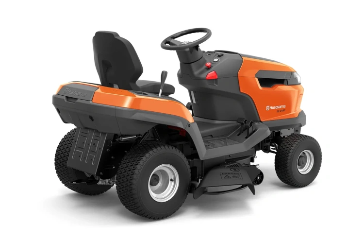 Traktor TS 215T Husqvarna w kolorze pomarańczowym z szarymi akcentami, ukazany z boku. Widoczne duże koła z bieżnikiem oraz wyprofilowane siedzenie z oparciem. Na panelu umieszczone są dźwignie i przyciski sterujące. Tło jasne, neutralne.