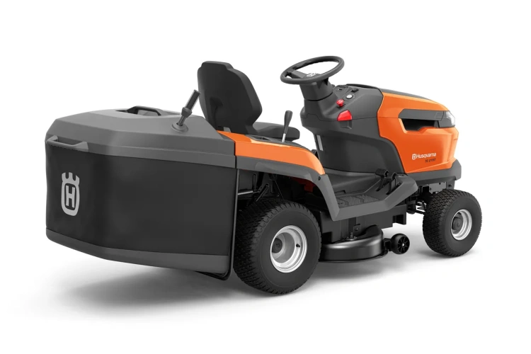 Pomarańczowy traktor Husqvarna TC 215T z szarymi akcentami, widok z boku na siedzisko, kierownicę, panel sterowania oraz duży tylny zbiornik na trawę. Kółka owalne widoczne z boku.