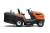 Traktor TC 215T Husqvarna w kolorze pomarańczowym z szarymi akcentami, widoczny z boku. Posiada duże koła, siedzisko oraz panel sterujący. Z przodu umieszczony kosz na trawę, a z tyłu znajduje się silnik. Plastikowa obudowa o matowej fakturze.
