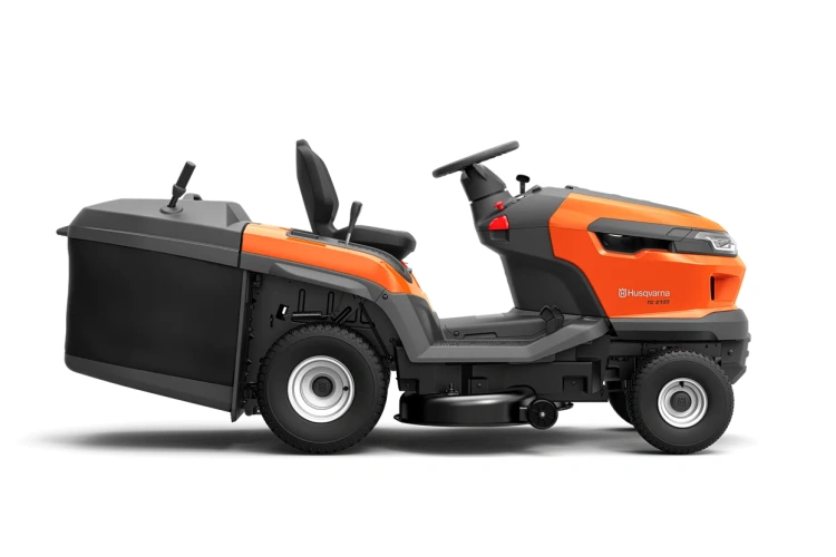 Traktor TC 215T Husqvarna w kolorze pomarańczowym z szarymi akcentami, widoczny z boku. Posiada duże koła, siedzisko oraz panel sterujący. Z przodu umieszczony kosz na trawę, a z tyłu znajduje się silnik. Plastikowa obudowa o matowej fakturze.