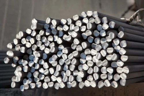 Zestaw stalowych prętów o sześciokątnych końcach, ułożonych równolegle. Pręty mają metaliczny połysk i są w kolorze ciemnosrebrnym. Widok z góry, z bliska, ukazuje równą powierzchnię oraz wyraźne detale na końcówkach.