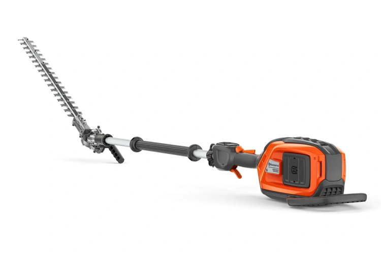 Nożyce do żywopłotu na wysięgniku Husqvarna 525iHE3 z ostrzem w stylu prostokątnym, w kolorze pomarańczowym i szarym, z ergonomiczną rączką i przyciskiem uruchamiania. Prezentowane z boku, ukazujące długi wysięgnik. Tło proste, czarne.