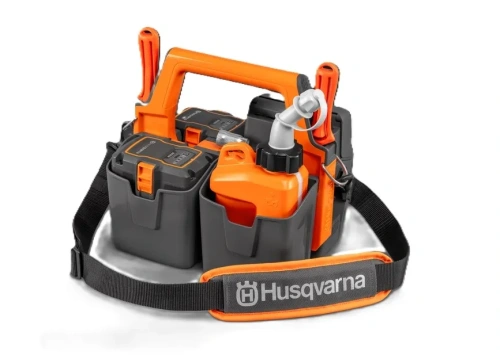 Skrzynka na akumulatory do pilarki Husqvarna w kolorze szaro-pomarańczowym. Z przodu widoczne są zbiorniki na akumulatory oraz czerwony zbiornik na paliwo, zamontowane w praktycznej torbie z uchwytem. Logo Husqvarna na pasku ułatwia transport.