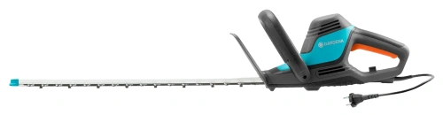 Elektryczne nożyce do żywopłotu Gardena ComfortCut 600/55 w kolorze szaro-niebieskim. Produkt widoczny z boku, z długim ostrzem do cięcia. Uchwyt ergonomiczny w czarnej fakturze. Kabel zasilający z wtyczką umieszczony z tyłu urządzenia.
