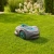 Szary robot koszący Gardena Sileno SMART 1200 na zielonym trawniku z niebieskimi detalami. Widoczny panel sterujący, w tle kwiaty i krzewy ogrodowe.