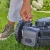 Radar antykolizyjny Gardena smart w czarnym kolorze, montowany na robocie. Widoczna dłoń mężczyzny chwytająca przewód, z zielonymi trawami w tle. Ujęcie z boku, pokazujące boczną część urządzenia i sposób użytkowania.