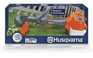 Zabawka dla dzieci wykaszarka Husqvarna w kolorze pomarańczowym i szarym, widoczna z boku na prostopadłym tle, z detalami określającymi ergonomiczny uchwyt i tarczę tnącą. Logo Husqvarna na korpusie, akcesoria do zabawy przy rozkładzie.