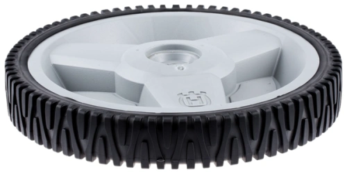 Koło kosiarki LB 155S Husqvarna, plastikowa osłona w kolorze szarym z żłobieniami, czarnym gumowym bieżnikiem. Ujęcie z boku, widoczne logo Husqvarna w centralnej części. Produkt leży na płaskiej powierzchni, gotowy do montażu.