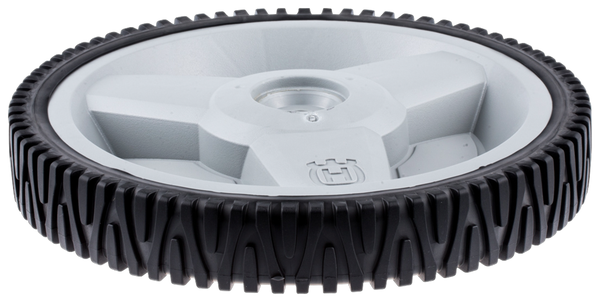 Koło kosiarki LB 155S Husqvarna, plastikowa osłona w kolorze szarym z żłobieniami, czarnym gumowym bieżnikiem. Ujęcie z boku, widoczne logo Husqvarna w centralnej części. Produkt leży na płaskiej powierzchni, gotowy do montażu.