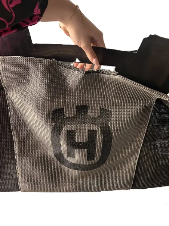 Kosz na trawę do traktora Husqvarna CTH 174, czarno-szary, trwały materiał, z otwartą przestrzenią do zbierania trawy. Z boku logo Husqvarna, trzymany w dłoni.