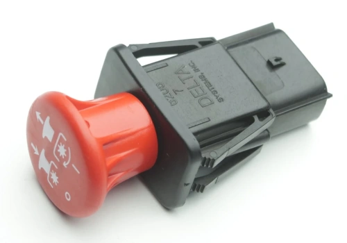 Wyłącznik kosiarki Husqvarna Z560X z czerwonym pokrętłem i ikonami działania, pokazany w pozycji leżącej z widocznym czarnym korpusem i symbolami kierunku włączania na pokrętle.