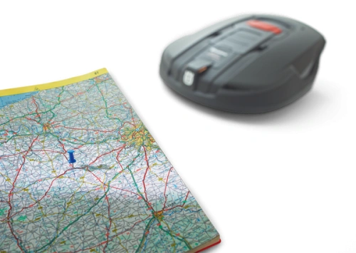 Moduł komunikacji GPS Automower Solar Hybrid Husqvarna, szary, o opływowym kształcie, leży na mapie drogi z widocznymi trasami i oznaczeniami. Ujęcie z góry ukazuje szczegóły produktu oraz fragment mapy ułatwiający lokalizację.
