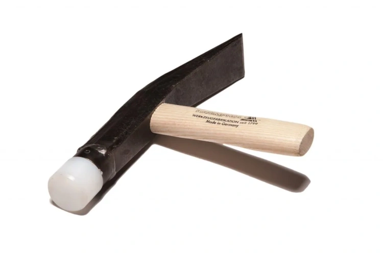 Młotek brukarski 2 kg z nasadą PCV, z drewnianym uchwytem. Narzędzie leży na białym tle, ukazując ciemnoszary, matowy metalowy łeb oraz przezroczystą nasadę PCV. Widoczne napisy na uchwycie: Made in Germany.