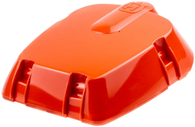 Pokrywa filtra pilarki Husqvarna 385, 390XP w intensywnym pomarańczowym kolorze, o gładkiej fakturze, zamontowana w pozycji leżącej. Widoczne logo Husqvarna oraz delikatne żłobienia po bokach ułatwiające chwyt. Tło jednolite, białe.