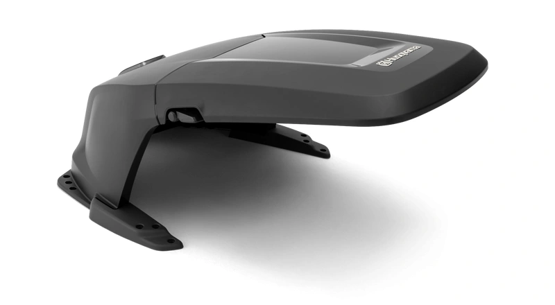 Domek osłony dla Automower Husqvarna serii 400 w kolorze szarym, z widocznym wejściem. Produkt stoi na płaskiej powierzchni, z wyraźnym logo Husqvarna na górze. Materiał plastikowy, odporny na warunki atmosferyczne.