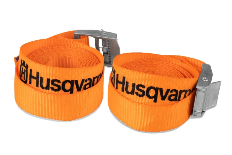 Pas zabezpieczający z klamrą Husqvarna w pomarańczowo-czarnej kolorystce, wykonany z materiału. Z przodu widoczna metalowa klamra oraz Czarny napis Husqvarna. Produkt leży poziomo na jasnym tle.