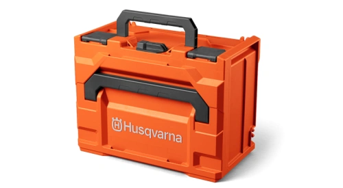Skrzynka na akumulatory Husqvarna w kolorze pomarańczowym z czarnym uchwytem. Produkt zamknięty, widoczny z przodu. Solidny plastikowy materiał, prostokątny kształt z wyraźnym logo Husqvarna na wieczku.