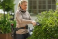 fotografia przedstawia kobietę która wykonuje prace porządkowe w swoim ogrodzie za pomocą sekatora husqvarna. Precyzyjnie przycina widoczny przed nią krzew.