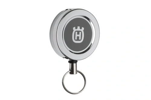 Uchwyt z metalową rolką sprężynową w kolorze metaliczno-szarym. Produkt w pozycji wiszącej z widocznym logo Husqvarna na górze. Idealny do mocowania narzędzi.