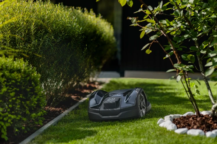 Automower® 305E NERA, robot koszący Husqvarna, w kolorze grafitowym. Ujęty podczas pracy w ogrodzie z wąskimi przejściami. Robot pokazany jest od strony frontalnej.