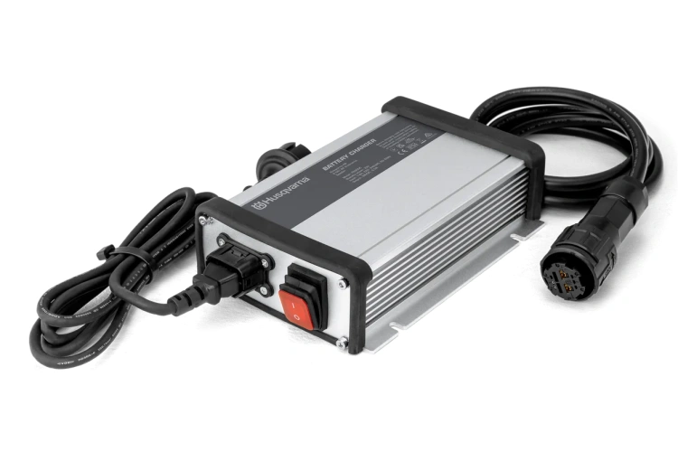 Ładowarka PS300C Husqvarna, czarna, prostokątna, z logo na obudowie. Wtyczka z kablami do ładowania. Ustawiona poziomo na jednolitym tle, idealna do ładowania kosiarek samojezdnych.