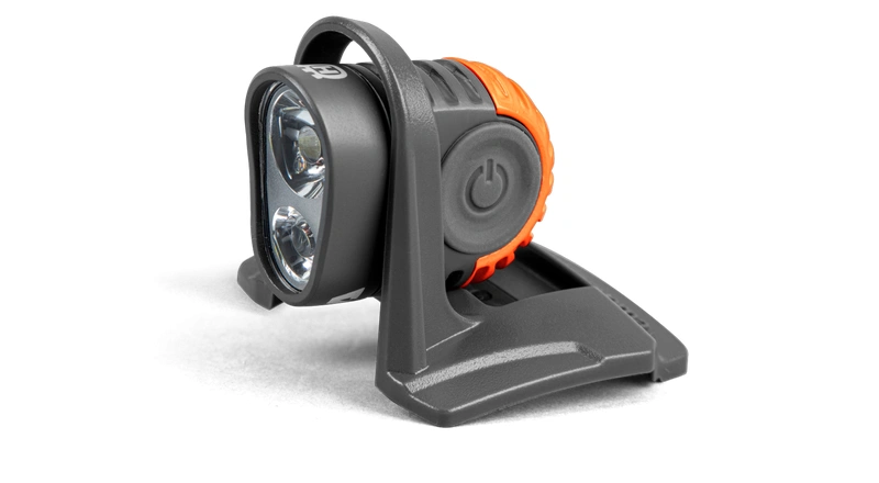 Latarka z akumulatorem do kasku Technical Husqvarna, w kolorze czarno-pomarańczowym, widoczne lampki i mocowanie, ujęcie z boku, widoczny włącznik latarki,