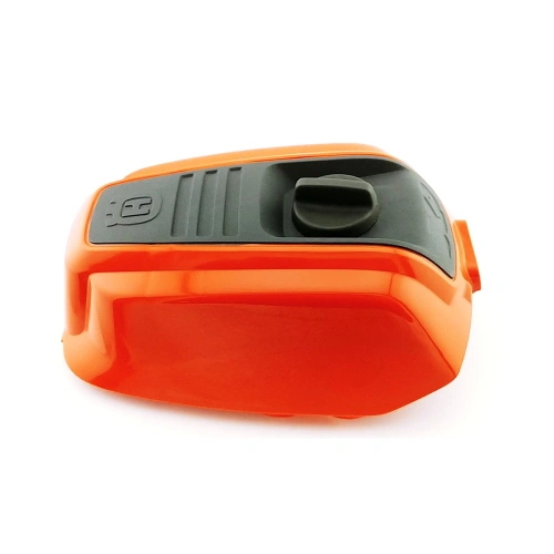 Pomarańczowa, plastikowa obudowa filtra powietrza pilarki 543 XP Husqvarna z szarym panelem na górze. Na tym panelu znajduje się pokrętło/przełącznik oraz wytłoczone logo Husqvarna, Widok z boku, na jasnym tle,