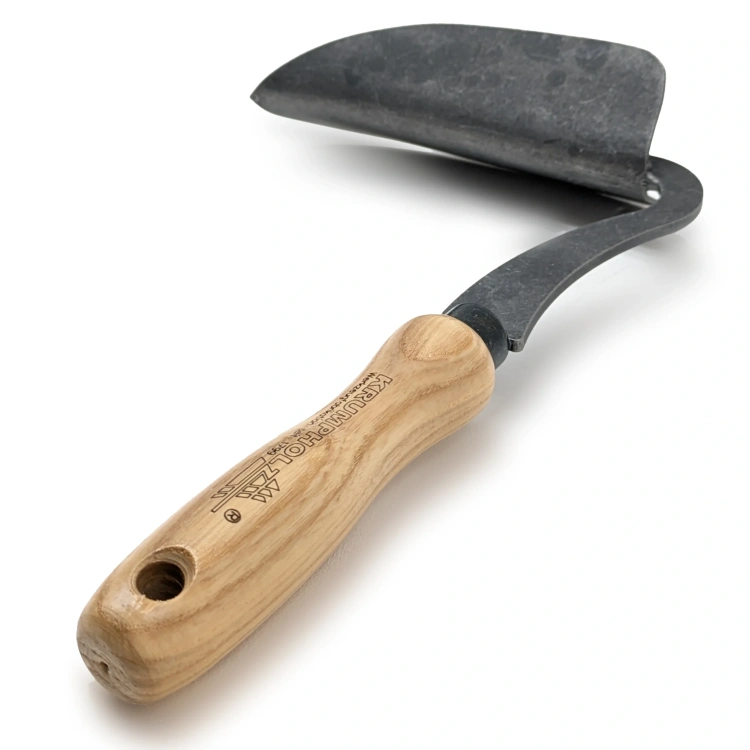 Motyczka zakrzywiona Krumpholz z  wygiętym ostrzem, wykonana z czarnej stali. Drewniana rączka z ergonomicznie uformowanym uchwytem. Produkt leży poziomo na jasnym tle, co podkreśla jego kształt i jakość materiałów.