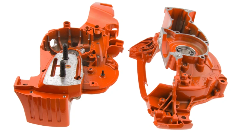 Zespół skrzyni korbowej pilarek Husqvarna 570 w pomarańczowej obudowie, boczny widok z zamontowanymi drzwiami. Widoczne metalowe śruby i uchwyty, na białym tle podkreślającym detale.