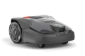 Automower 308v Husqvarna to szary robot koszący z widoczną kamerą na froncie i logiem Husqvarna. Aerodynamiczny kształt, pokazany z boku na płaskiej powierzchni.