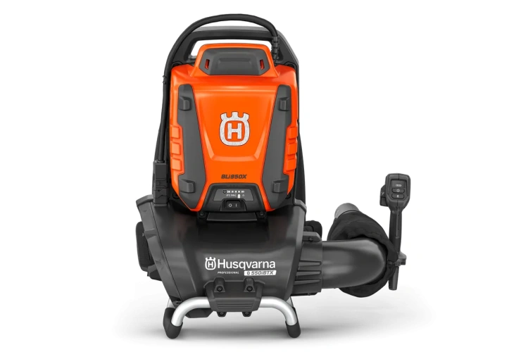 Akumulatorowa dmuchawa 550iBTX w kolorze pomarańczowym i szarym z ergonomiczną rączką. Widok z boku, pokazujący podłogowy kabel zasilający oraz akumulator zamocowany na pasku. Produkt w użyciu, na jednolitym tle.