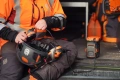 Adapter akumulatorowy Husqvarna 40-USB150X w kolorze pomarańczowym, widoczny podczas użytkowania w pracy.